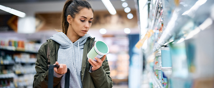 Persoon in een supermarkt bekijkt een productverpakking in het schap met levensmiddelen.