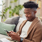 Persoon die op een bank zit en een smartphone gebruikt, met een laptop op schoot