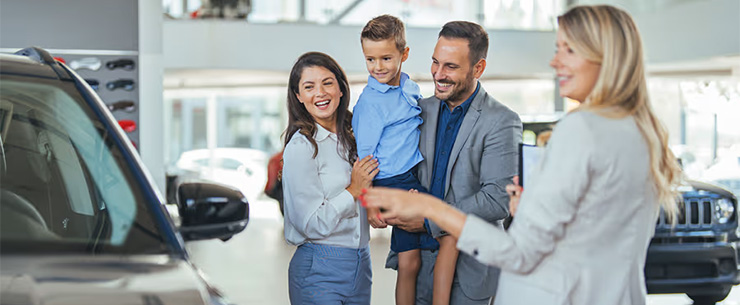 Gezin staat in een showroom naast een auto terwijl een verkoper uitleg geeft