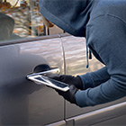 Persoon met handschoenen gebruikt een apparaat bij het portier van een geparkeerde auto.