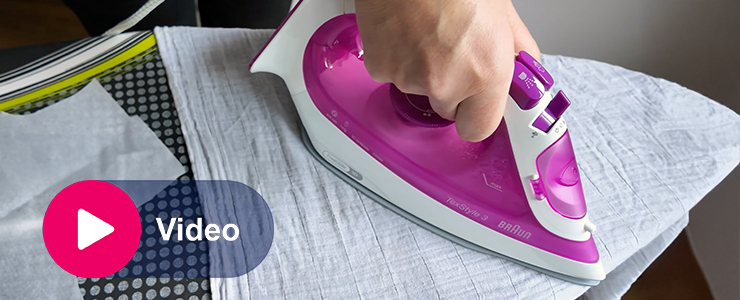 Hand die een roze strijkijzer over een licht overhemd beweegt, met video-icoon