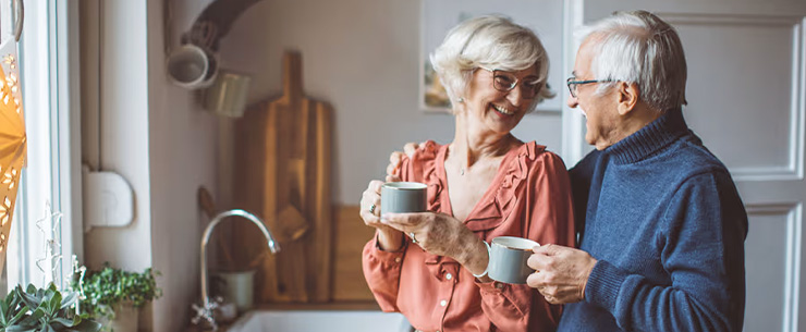 Oudere man en vrouw staan in een keuken en houden elk een kop koffie vast
