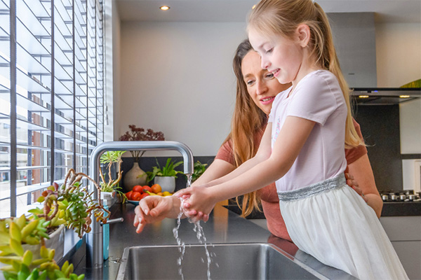 Vrouw en kind bij aanrecht in keuken, kijkend naar geopende keukenkast met cv-installatie