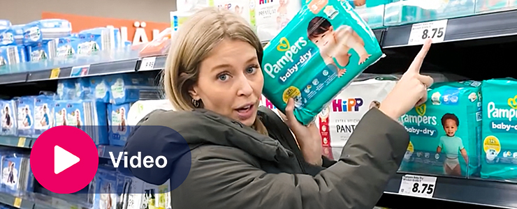 Vrouw in supermarkt wijst naar prijskaartje terwijl zij pak luiers vasthoudt in winkelschap