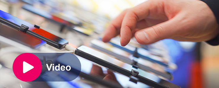 Hand wijst naar smartphones die naast elkaar op displaystandaard liggen in winkel.