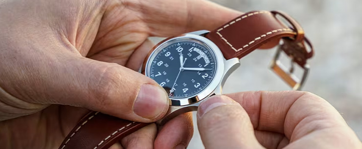 Iemand die de tijd verzet op een polshorloge met bruine leren band..