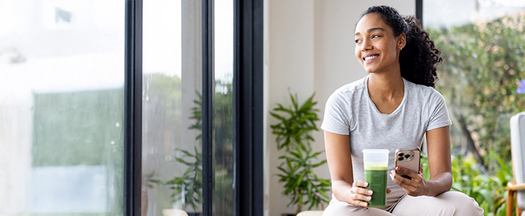 Vrouw zit bij het raam en drinkt een smoothie