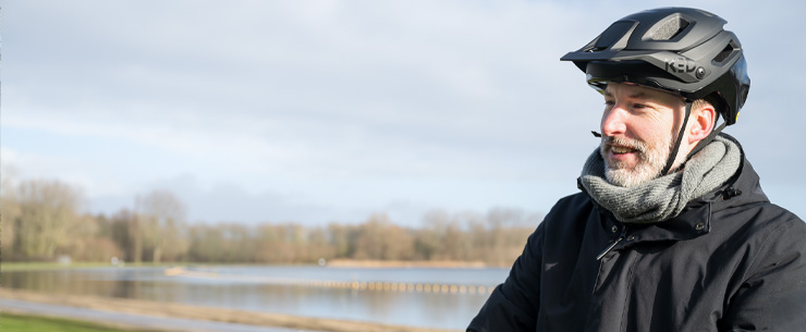 Man met fietshelm en sjaal staat buiten bij het water.