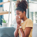 Vrouw zit op een bank en houdt een tissue voor haar neus.