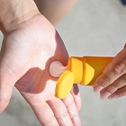 Hand smeert zonnebrandcrème uit een gele tube in een open handpalm.