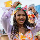 Vrouw met gevlochten haar en zonnebril op het hoofd heft haar armen op tijdens een buitenevenement