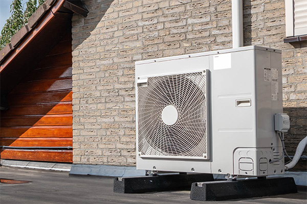 Buitenunit van een warmtepomp naast een stenen woning.