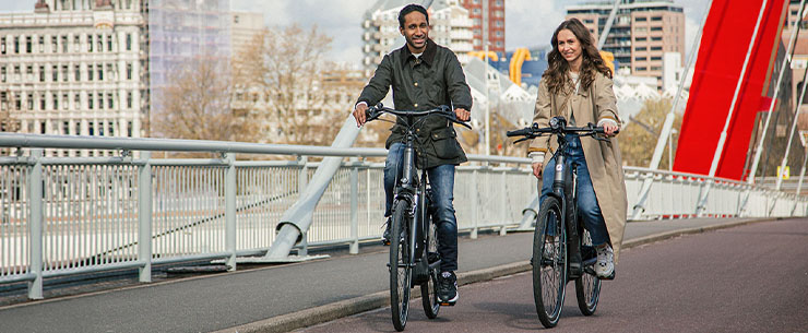 Twee personen fietsen naast elkaar op een brug in een stedelijke omgeving