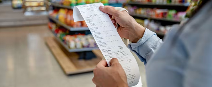 Handen houden een kassabon vast in een supermarkt.