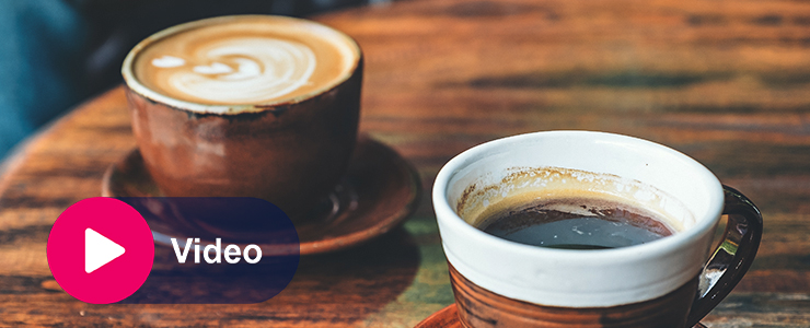Twee koppen koffie op een houten tafel met een videoknop in beeld