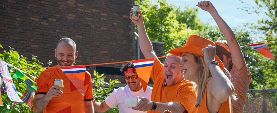 Groep personen in oranje kleding viert buiten onder vlaggenlijnen
