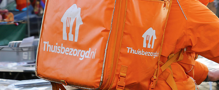 Maaltijdbezorger van Thuisbezorgd met bezorgtas bij een woning