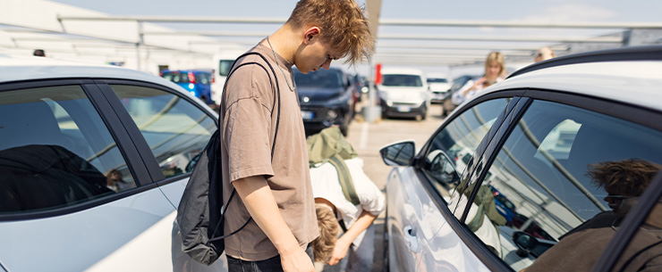 Jongen staat tussen geparkeerde auto’s en bekijkt schade aan een voertuig