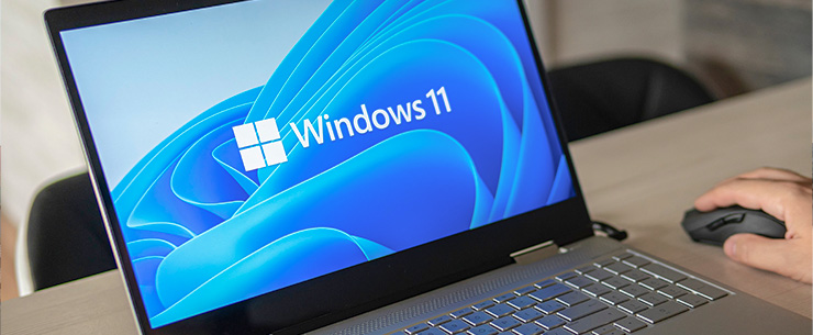 Laptop met het Windows 11-logo op het scherm en een hand op een computermuis
