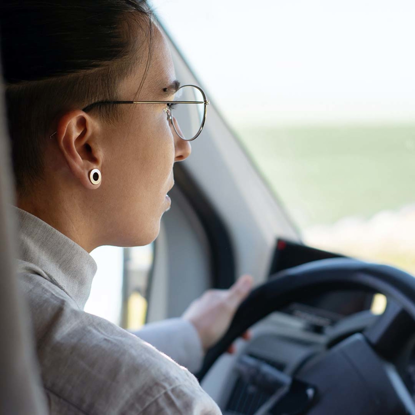 Frau mit runder Brille beim Autofahren, Profilansicht, Hand am Lenkrad.