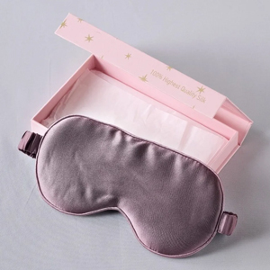 Mauve satin sleep eye mask with adjustable strap resting on open pink gift box lined with tissue paper