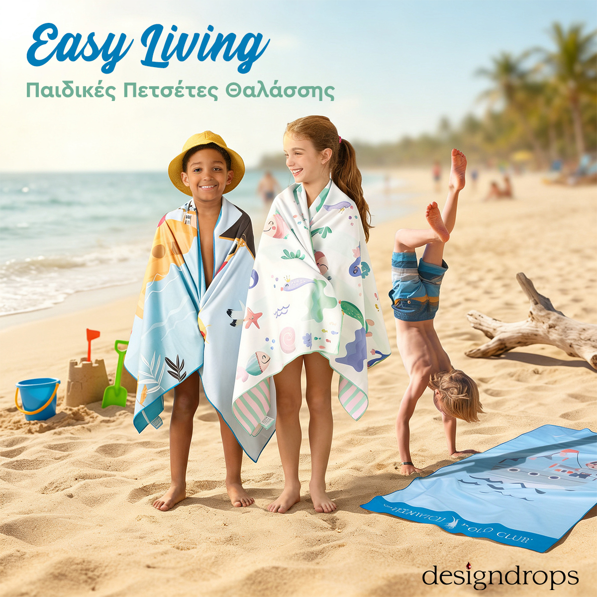 Three children on a sunny beach: two wrapped in sea‑themed towels beside a sandcastle, a third doing a handstand by a beach towel.