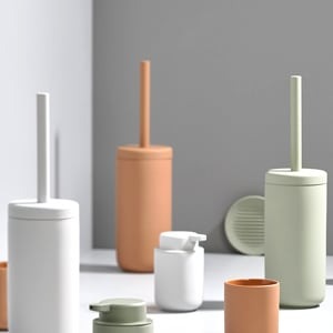 Minimalist pastel-coloured bathroom accessories set — mint, terracotta and white toilet brushes, soap dispensers and containers on a grey surface