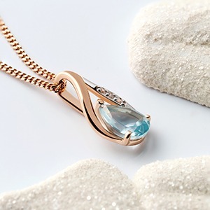 Rose-gold pendant necklace with pear-shaped aquamarine and small diamonds on a fine chain, styled on white sand