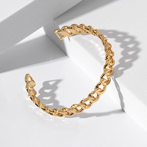 Gold chain-link open cuff bracelet on white geometric display with polished finish and soft shadow