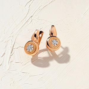 Pair of rose-gold hoop earrings with round halo diamond centres on textured cream background