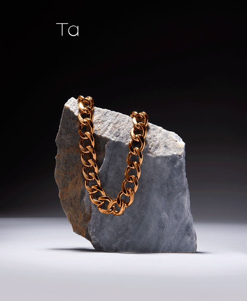 Gold chain draped over a grey stone on a tiled promotional poster with Greek text, jewellery product image