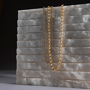 Gold chain necklace draped over stacked white marble slabs on dark background