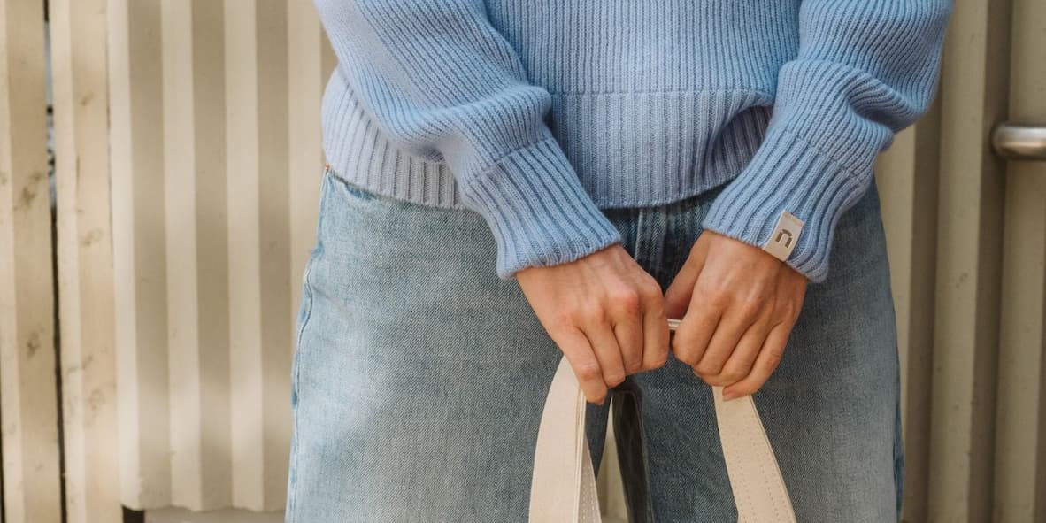 Kuva käsistä, joka kantaa kangaskassia. Päällä vaalensininen Kieppi neule.