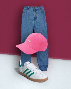 Blaue Jeans, pinke Kappe und weiße Turnschuhe mit grünen Streifen vor einem roten Hintergrund.