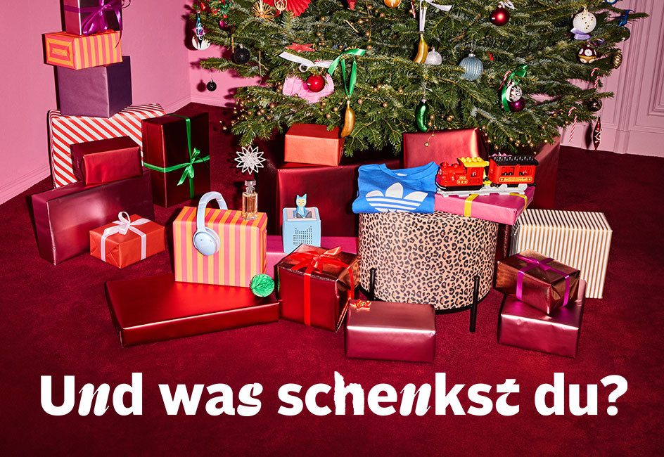 Ein Weihnachtsbaum mit vielen bunt verpackten Geschenken darunter. Text: "Und was schenkst du?"