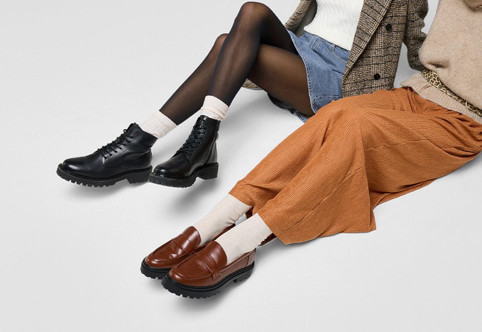 die Beine zweier Frauen in Boots und Halbschuhen vor grauem Hintergrund