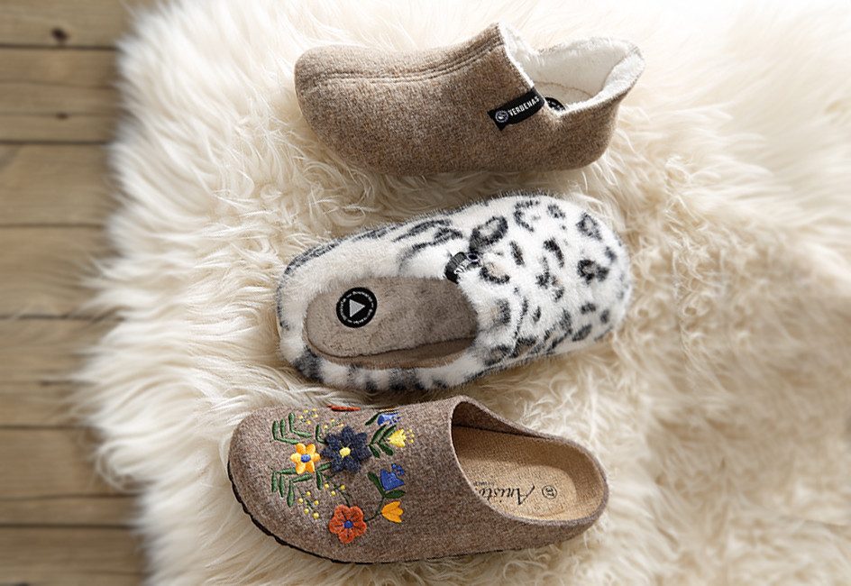 drei verschiedene Hausschuhe aus Plüsch und Filz liegen auf einem hellen Fell