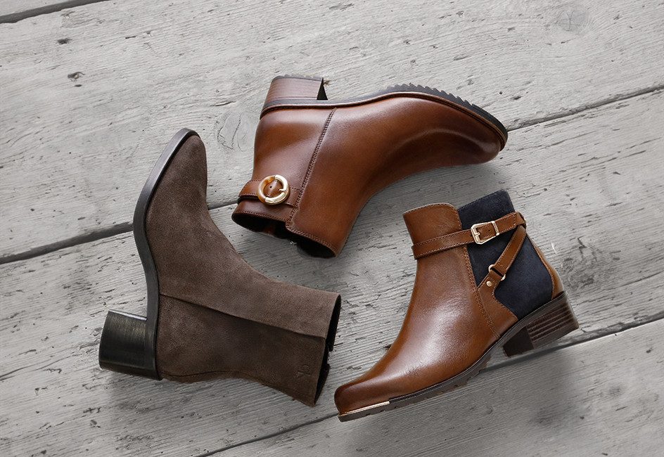 drei verschiedene Stiefeletten liegen auf grauem Holzboden