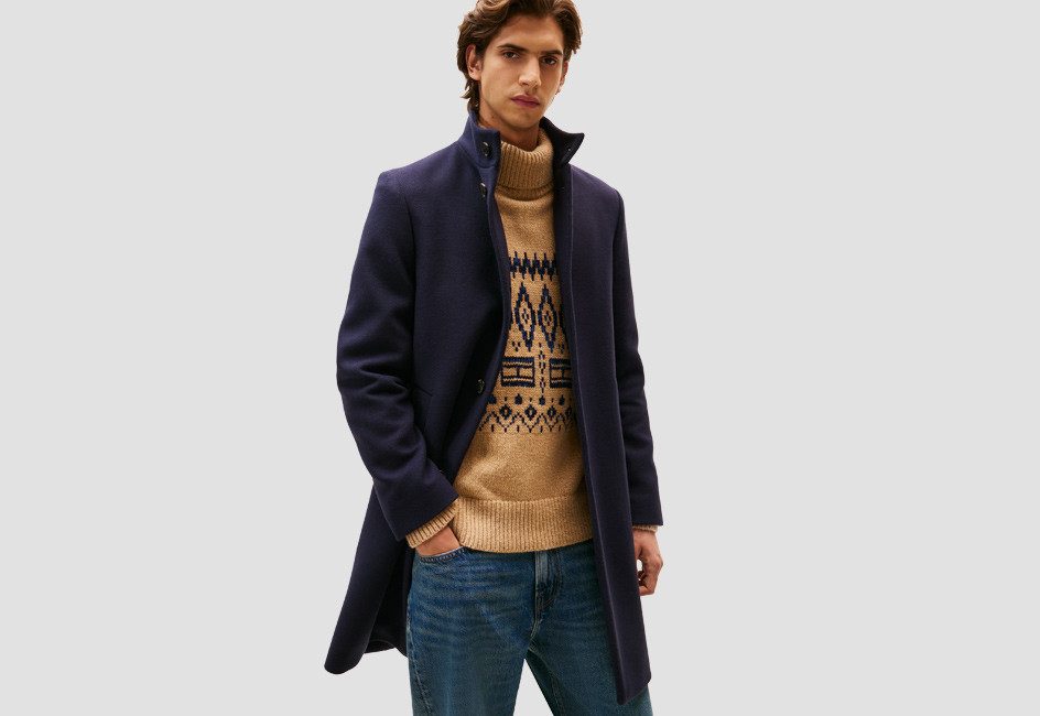 Mann in dunklem Mantel und gemustertem Pulli