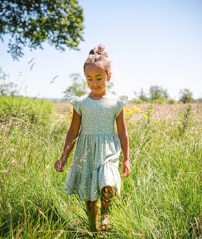 Ein Mädchen in einem Sommerkleid in der Farbe Mint spaziert durch ein Feld