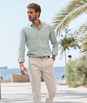 Mann in einem grün-weiß-gestreiftem Langarmhemd in Leinenoptik und einer beigen Hose