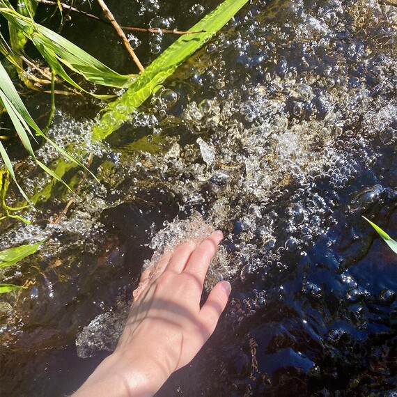 Kuvassa on onkäsi upotettuna kuplivaan puroon.