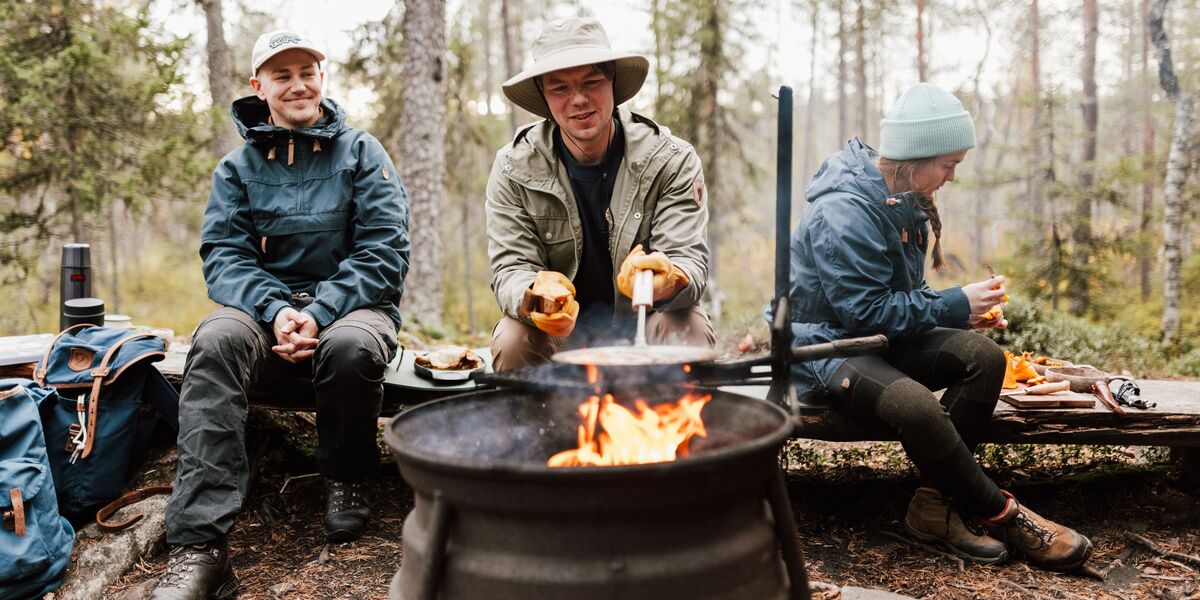 Kolme ihmistä istumassa leirinuotiolla metsässä.