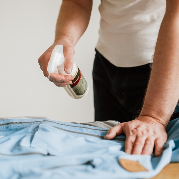 Käsi suihkuttamassa kuorivaatteet kyllästysainetta kuoritakkiin