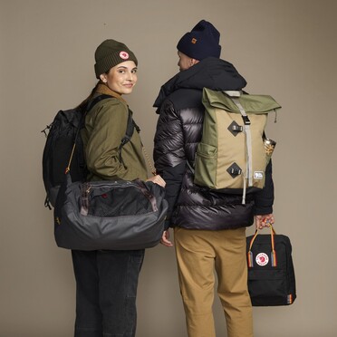 Kaksi ihmistä kuvattuna studiossa. Heillä on käsissään paljon kasseja ja reppuja.