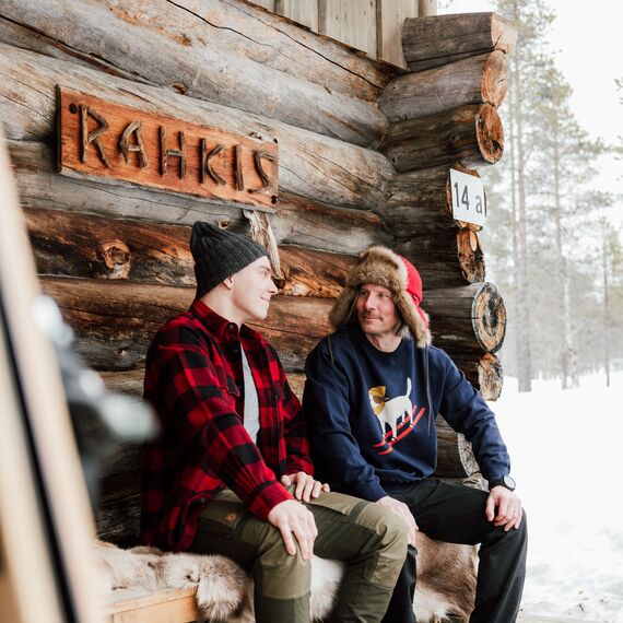 Mies ja poika istumassa mökin edustalla penkillä. He katsovat toisiaan ja hymyilevät