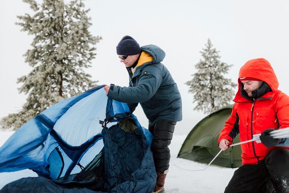Kaksi miest&auml; pystytt&auml;m&auml;ss&auml; telttaa talvimaisemassa