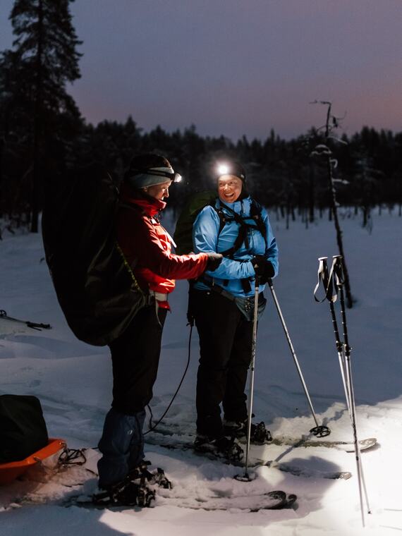 Kaksi naista katsomassa karttaa otsalamppujen avulla pime&auml;ss&auml;. Heill&auml; on jalassaan sukset.