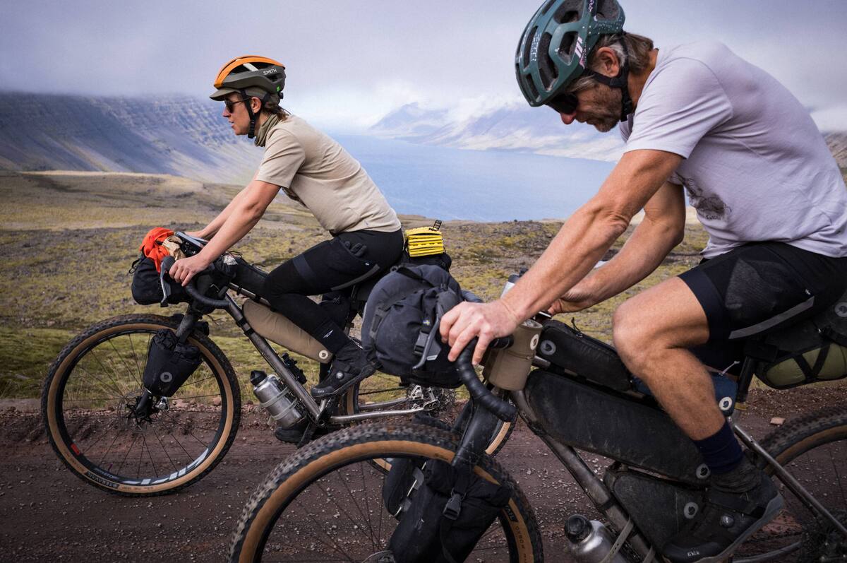 Nainen maastopy&ouml;r&auml;n edess&auml; aavikolla. H&auml;n katsoo kameraan ja hymyilee.