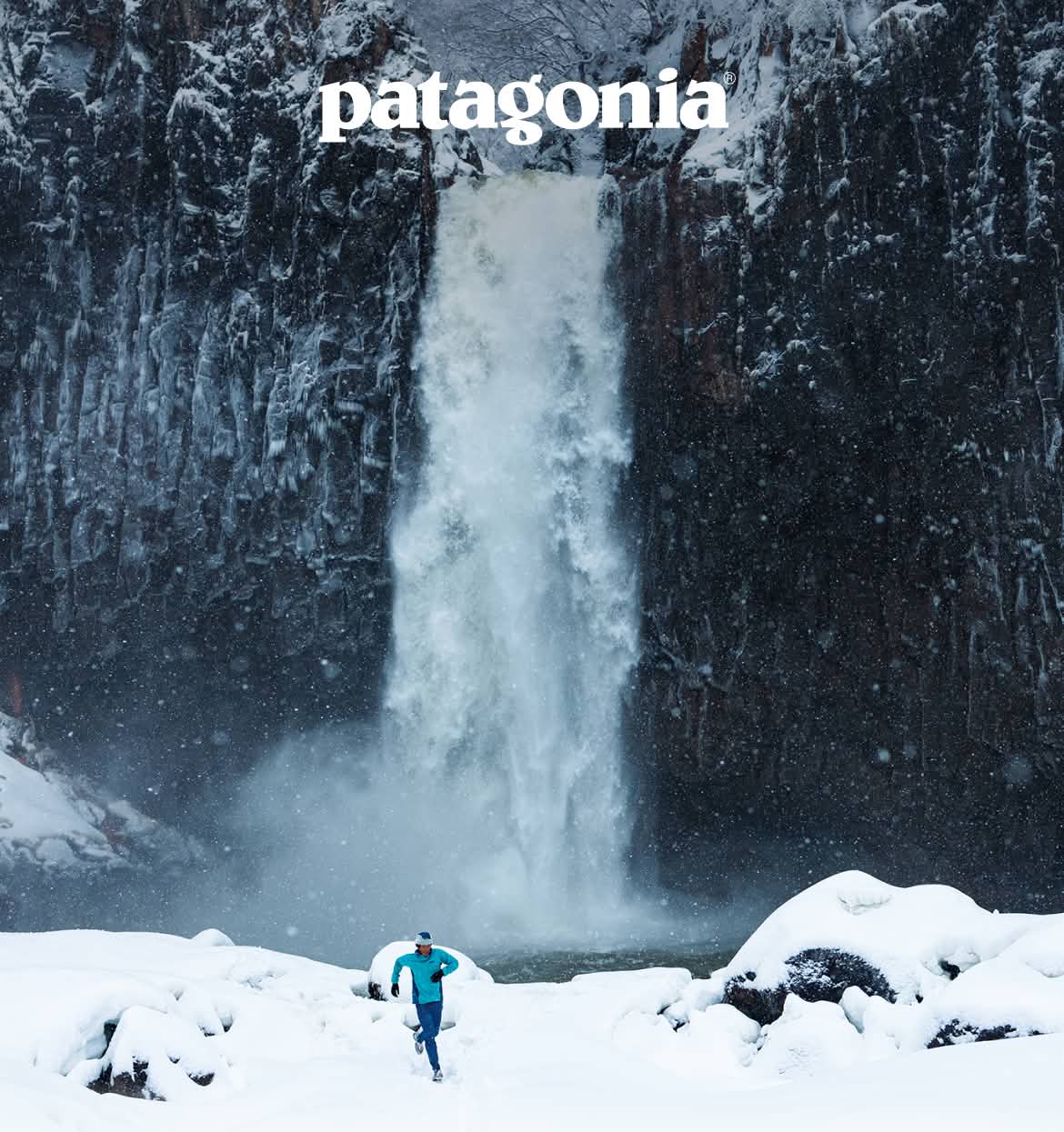 Patagonia.  A person runs past a waterfall in the snow.